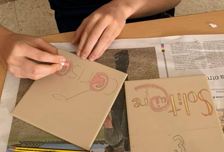 Élève décore des carreaux avec des craies céramiques. Atelier mosaïque en français